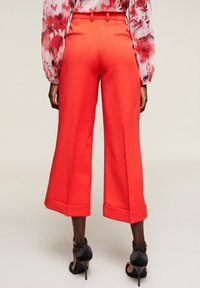 Klarröda vida byxor med skräddarsydd passform, med vikt kanter och en mjuk tygtextur, kombinerat med svarta högklackade skor.