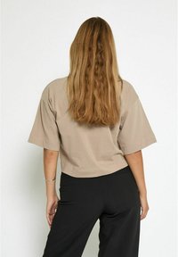 Short-sleeve, cropped t-shirt in light beige cotton. Soft texture with a relaxed fit, paired with black wide-leg pants.