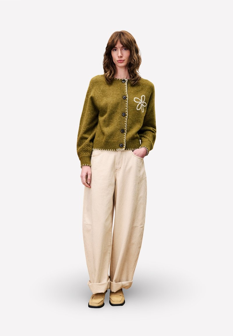 Groene gebreide cardigan met een bloemenborduursel, zes knopen, geribde manchetten, gecombineerd met beige wijde broek en beige schoeisel.