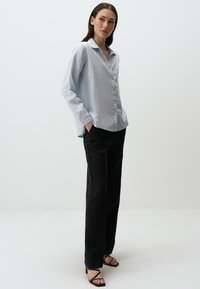 Lichtblauwe, lange mouwen overhemd met kraag en casual pasvorm, gecombineerd met zwarte recht gesneden broek en zwarte enkelbandhakken.