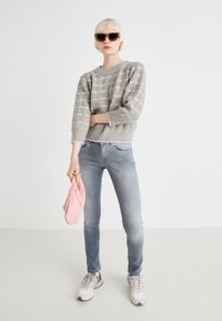 Un pull en maille grise avec un motif texturé, un jean skinny bleu clair, un sac à main pink, et des baskets grises, sur un fond uni.