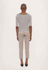 Haut rayé à manches longues crème et marine associé à un pantalon beige ajusté, présentant un design cintré et une longueur cropped. Chaussures plates noires.
