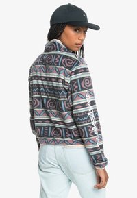 Fleece pullover in geometric patterns of pink, blue, and cream. Features a high collar and white branding on the left sleeve.