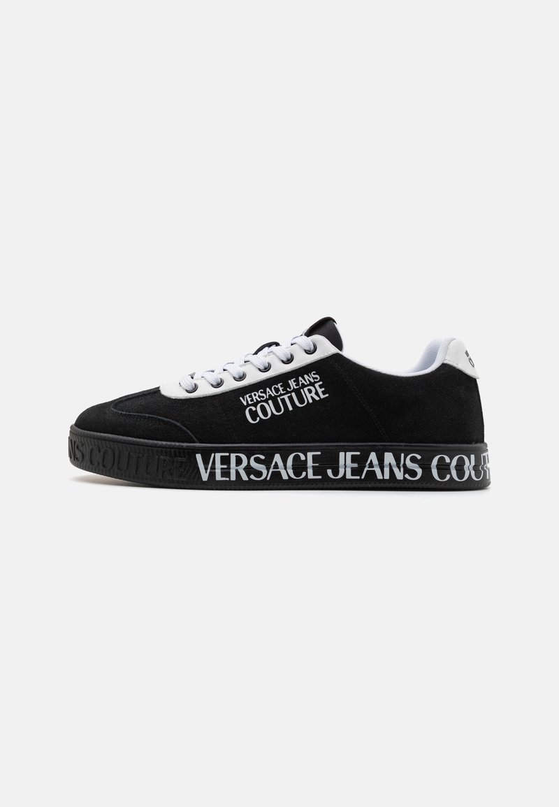 Sorte semskede sneakers med hvite snøringer og en hvit tåhette. Har en tykk svart såle med "VERSACE JEANS COUTURE" preget i hvitt.