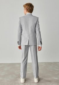 Completo grigio chiaro con giacca strutturata e pantaloni dritti. Caratterizzato da una texture liscia, bottoni neri e polsi di camicia bianca visibili.