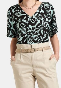 Top nero con scollo a V e maniche corte, decorato con un motivo astratto verde menta, abbinato a pantaloni beige a vita alta e una cintura beige con borchie.