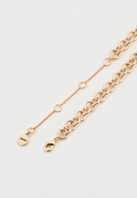 Βραχιόλι αλυσίδα σε χρυσή απόχρωση με διασυνδεδεμένους οβάλ κρίκους, κούμπωμα σε σχήμα αστακού και μικρή στρογγυλή ετικέτα με χαραγμένο το "DKNY".