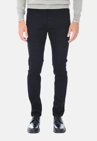 Jeans in denim nero, slim fit, con una texture liscia e senza decorazioni visibili, abbinati a scarpe in pelle nera lucida.