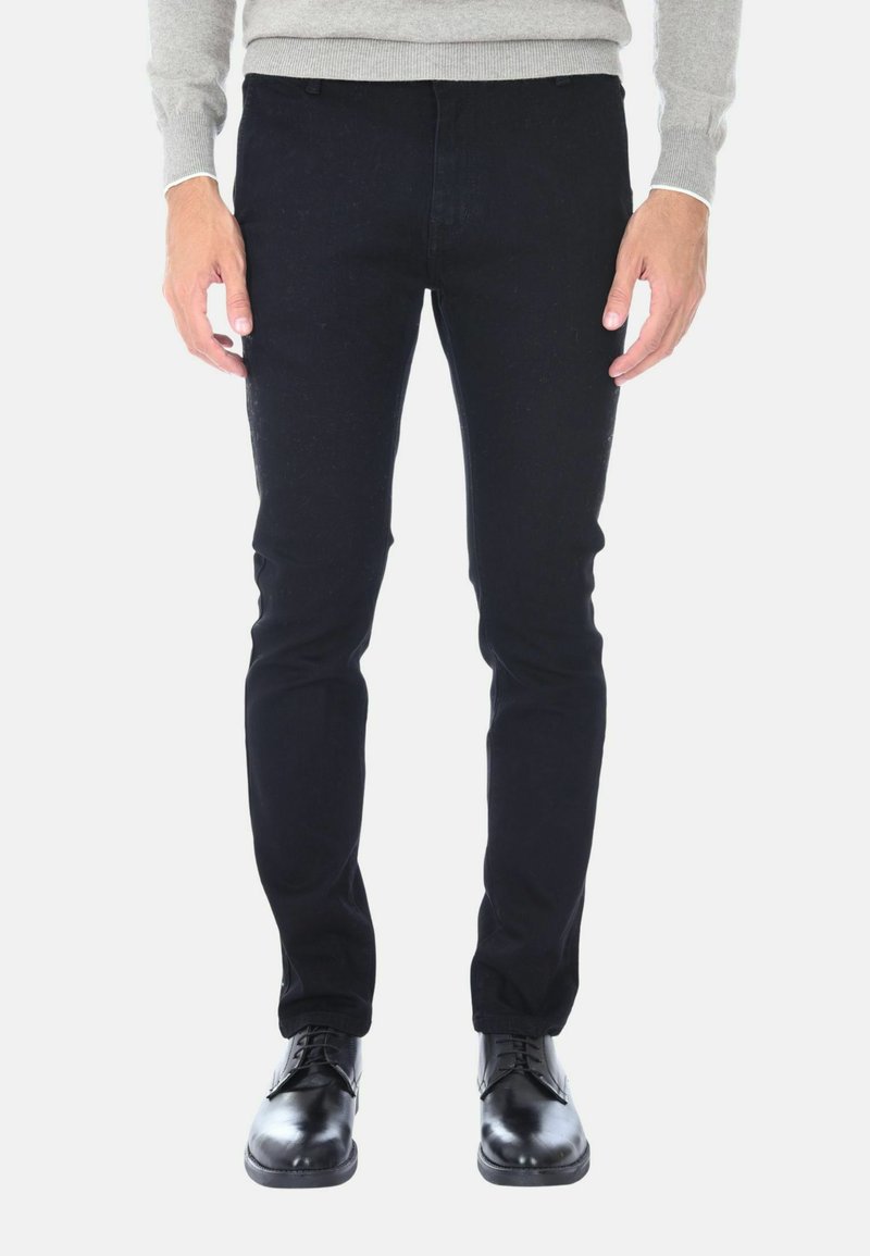 Jeans in denim nero, slim fit, con una texture liscia e senza decorazioni visibili, abbinati a scarpe in pelle nera lucida.