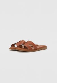 Brown leather slide sandals with two cut-out design panels, white stitching accents, and a flat rubber sole.