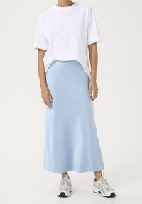 Weißes übergroßes T-Shirt kombiniert mit einem leichten, pastellblauen Satin-Maxirock, ergänzt durch graue und weiße Sportschuhe.