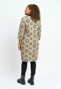 Beige keskitetty mekko, jossa on suuria mustia pyöreitä kuvioita, kolmostakki hihat ja rento malli, yhdistetty mustiin legginsseihin ja saappaisiin.