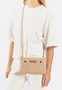 Lichtbeige leren schoudertas met gouden hardware accenten, decoratieve stiksels en een getextureerd voorpaneel. Verstelbare schouderband.
