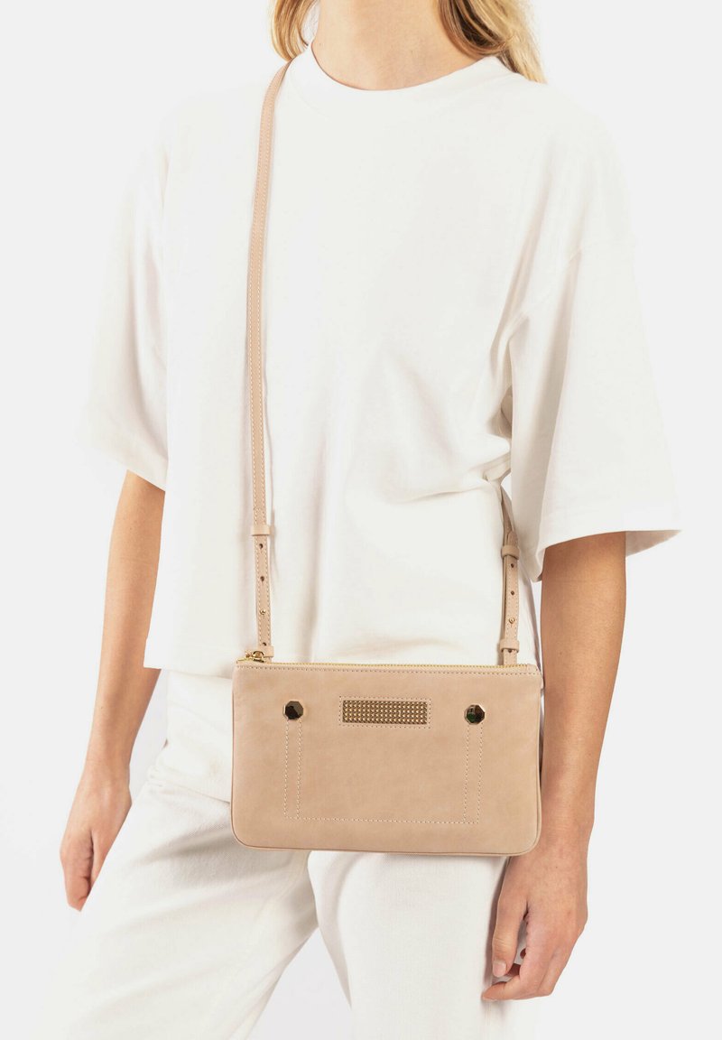Lichtbeige leren schoudertas met gouden hardware accenten, decoratieve stiksels en een getextureerd voorpaneel. Verstelbare schouderband.