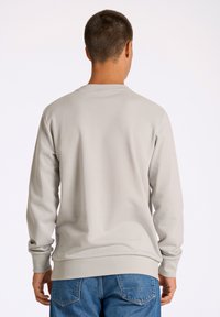 Sudadera gris claro de manga larga, con puños y dobladillo de canalé, diseño minimalista, combinada con jeans de mezclilla azules.