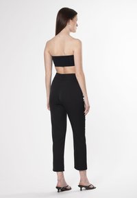 Zwarte strapless top gecombineerd met zwarte nauwsluitende broek, met een hoge taille en cropped lengte. De outfit wordt aangevuld met zwarte haksandalen.
