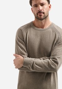 Lichtbruin, textuurpuls met geribbelde details op de schouders en manchetten. Ronde halsontwerp, lange mouwen, relaxte pasvorm.