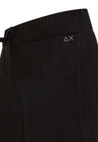 Pantaloni jogger neri a maglia con vita a coste, chiusura con coulisse e un piccolo logo bianco composto da forme geometriche.