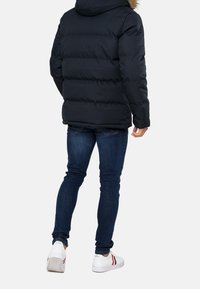Pufferjakke i marineblå med hætte og pelskant, med et quiltet mønster. Matchet med mørkeblå slim jeans og hvide sneakers med detaljer.