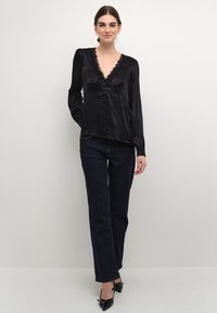 Blusa nera in satin con maniche lunghe, bordo in pizzo lungo il collo e chiusura a bottoni. Abbinata a pantaloni in denim scuro e décolleté neri a punta.