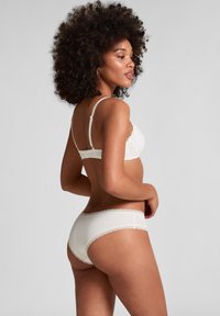 Jasna kremowa bielizna składająca się z biustonosza i majtek, wykonana z miękkiego materiału, z koronkowymi wykończeniami na brzegach, regulowanymi ramiączkami oraz gładkim, minimalistycznym designem.