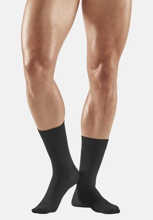 Black knee-high socks with a textured design, featuring a ribbed cuff and smooth finish. Socks are worn on muscular legs against a neutral background.