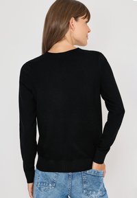 Maglione nero con maniche lunghe e scollatura rotonda. Presenta una texture liscia e una vita aderente. Indossato con pantaloni shorts in denim blu.