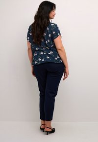 Marinblus med blommönster och korta ärmar, med vita och rosa blommor. Kombinerad med marinblå slim-fit byxor och svarta klacksandaler.