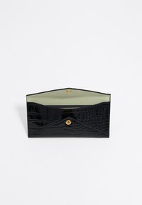Bolso de charol negro con un patrón de cocodrilo en relieve, que cuenta con un cierre de botón a presión dorado y un forro interior de color verde claro.