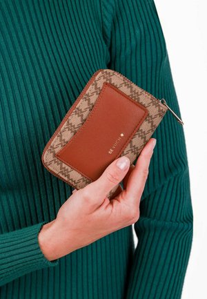 Hnědo-beige vzorovaná peněženka s hladkým koženým akcentem, s uzavíráním na zip a zlatým logem, držena v ruce před zeleným pozadím.