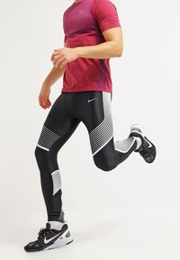 Leggings atléticos de rayas en blanco y negro con un diseño ajustado, combinados con una camiseta roja de manga corta en degradé y zapatillas de correr negras.