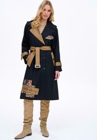 Czarny trencz z beżowymi akcentami, kieszeń w panterkę, detal z naszywką kwiatową, dwurzędowa konstrukcja, pasek w talii, beżowe kozaki do kolan.