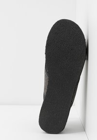 Semelle noire texturée d'une chaussure décontractée inclinée à la verticale contre un coin blanc de mur et de sol.