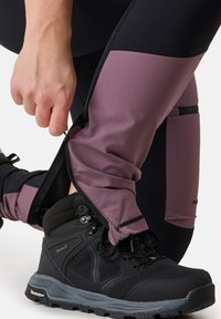 Svart vandringskänga med strukturerad sula, parat med högmidjade leggings som har en lila panel och en sidoficka med dragkedja.