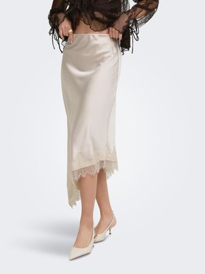Femme portant une jupe midi en satin crème avec bordure en dentelle et des escarpins slingback crème à bout pointu, associés à un top en dentelle noire.