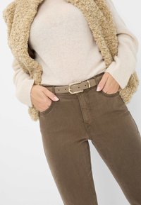 Bruine slim-fit broek van gladde stof, met een klassiek vijfzakken ontwerp. Een beige gestructureerde vest over een lichte trui.