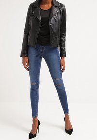 Svart skinnmotorcykeljacka över en svart topp, i kombination med blå skinny jeans med knäskador och svarta högklackade skor.