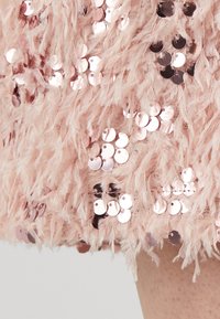 Tissu rose moelleux orné de paillettes dorées rose, créant une surface texturée et réfléchissante avec une apparence duveteuse.