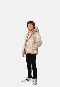 Giacca a vento imbottita beige con motivo e cappuccio, indossata sopra una felpa rosa chiaro e pantaloni neri. Presenta scarpe da ginnastica con un design nero.