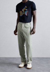 Czarna koszulka z kolorową grafiką roweru, jasnoszare spodnie i białe trampki. Gładki materiał, luźny krój, dopasowany fason.