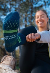 Calcetín de patrón hexagonal azul y verde con la marca "Danish Endurance", que presenta una tela texturizada y un ajuste ceñido, mostrado sobre un pie.