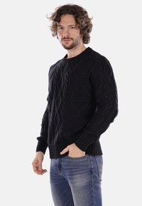 Maglione nero lavorato a maglia con un motivo a trecce testurizzato, collo rotondo e polsini a coste. Abbinato a jeans blu.
