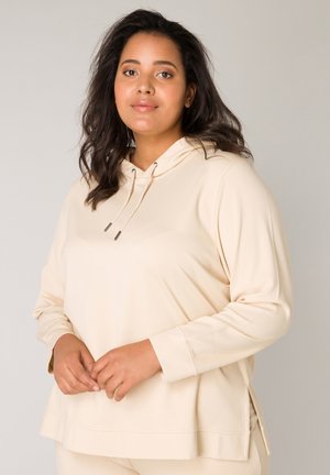 Beige hoodie gemaakt van zachte stof, met een ontspannen pasvorm, subtiele zijsplitsingen en verstelbare koorden bij de hals.