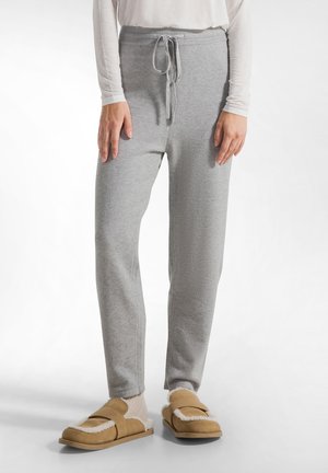 Pantaloni jogger grigi con vita regolabile e gambe affusolate, realizzati in tessuto morbido. Abbinati a ciabatte color sabbia con fodera pelosa.