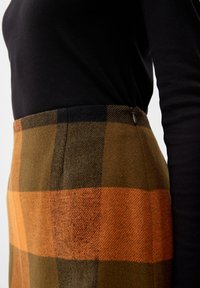 Wollen rok met een ruitpatroon in oranje, bruin en zwart. De stof heeft een gestructureerde afwerking en een ritssluiting aan de zijkant.