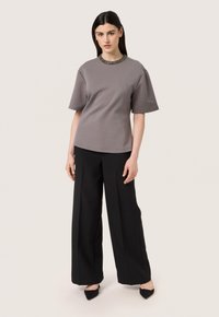 Top corto grigio a maniche corte con un colletto testurizzato e decorato, abbinato a pantaloni neri larghi e scarpe nere con punta.