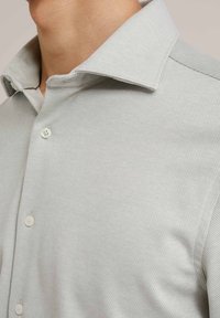 Lichtgrijze button-up shirt met een gestructureerde weving. Voorzien van een kraag, een enkele patch op de schouder en witte knopen.