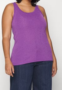 Lila ärmlös linne med glänsande textur, ribbat mönster och klassisk rund halsringning, kombinerat med mörkblå jeans.