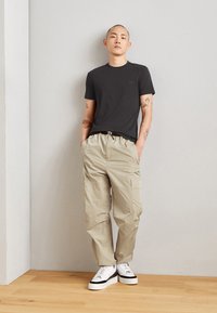 T-shirt nera in cotone abbinata a pantaloni cargo beige chiaro. Le calzature presentano una base bianca con accenti neri. Tessuto morbido e vestibilità comoda.