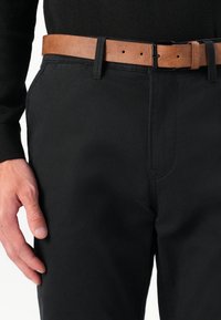 Schwarze Hosen mit glatter Textur und klassischer Passform. Kombiniert mit einem braunen Leder Gürtel, der eine rechteckige Metallschnalle zeigt.